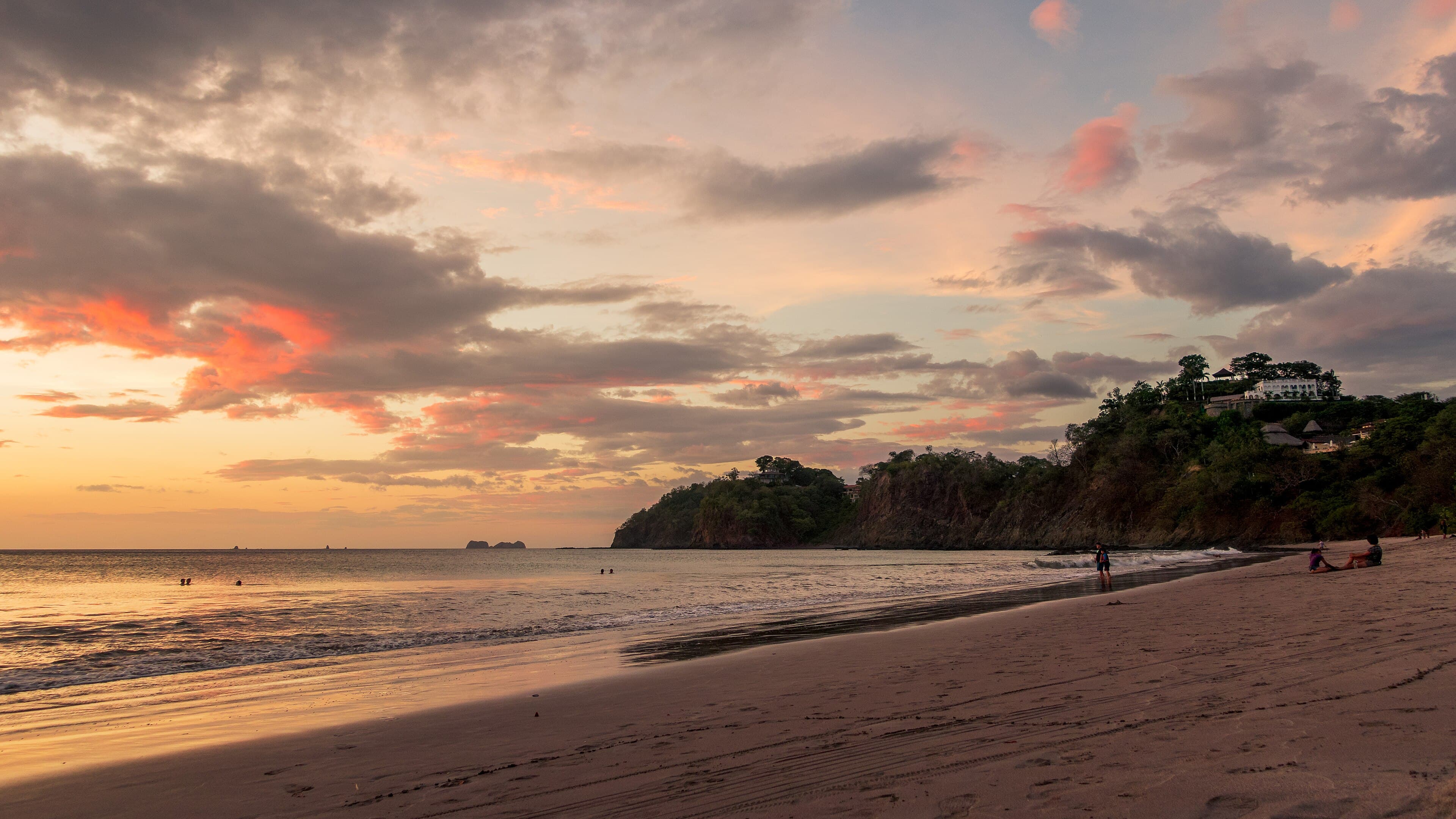 Sunset at Playa Flamingo: swimmers in calm water, the headland villas, and the Catalina Islands offshore