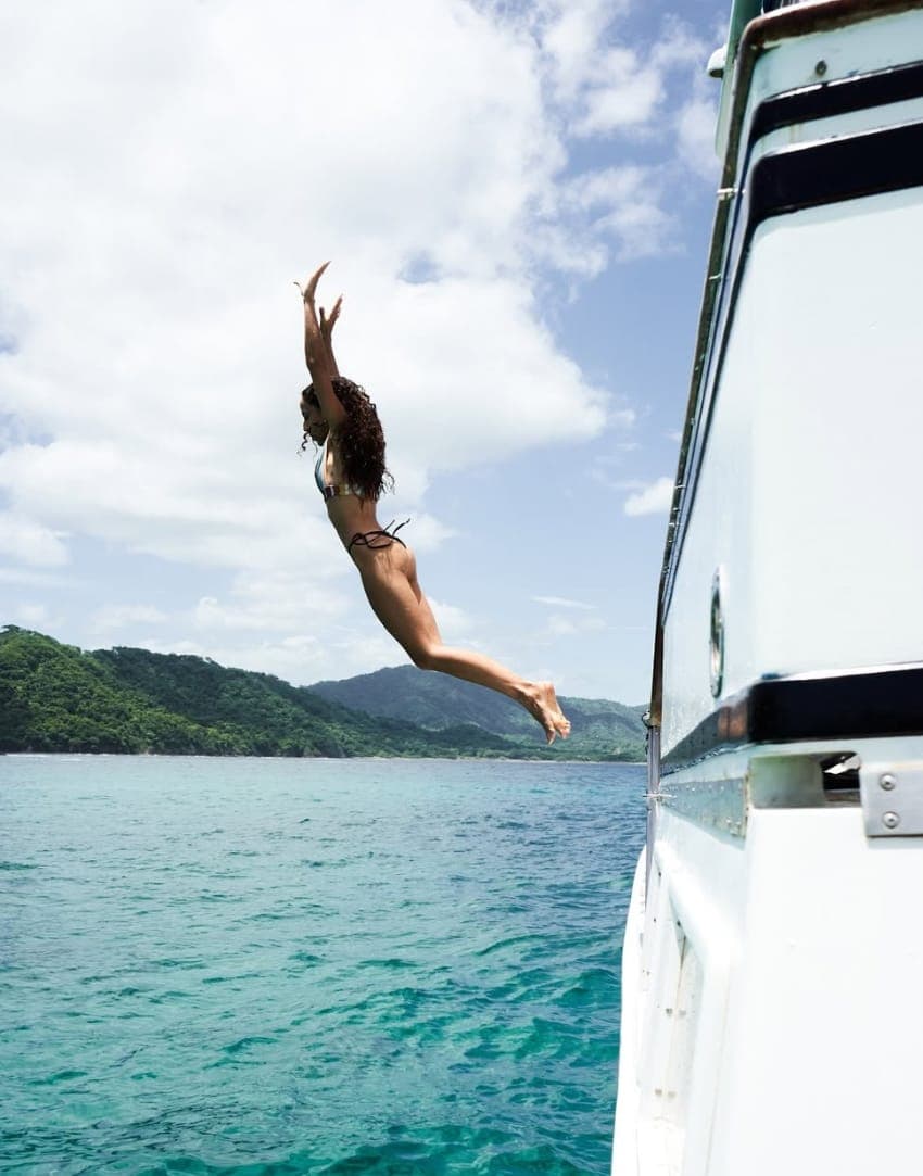A guest diving off the side of the boat into turquoise water below green hills