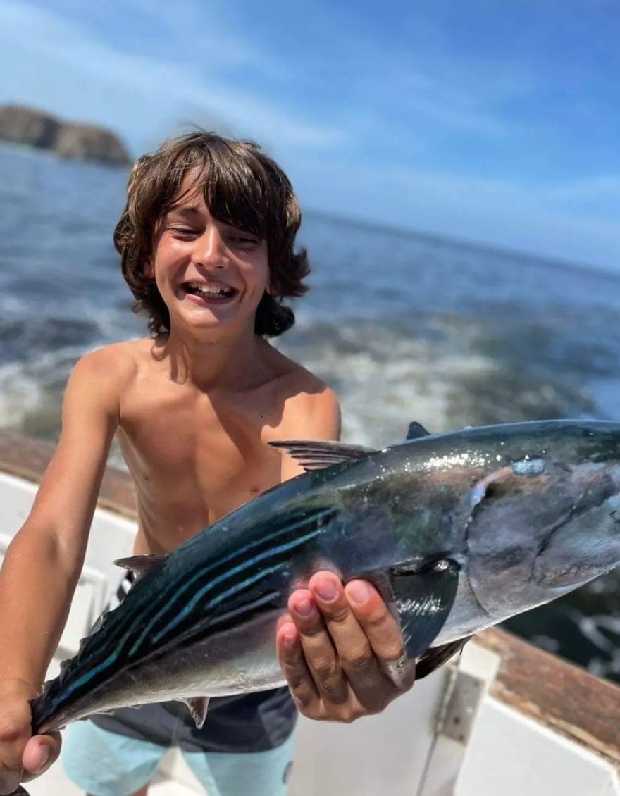 A grinning boy holding up a freshly caught tuna on the back deck