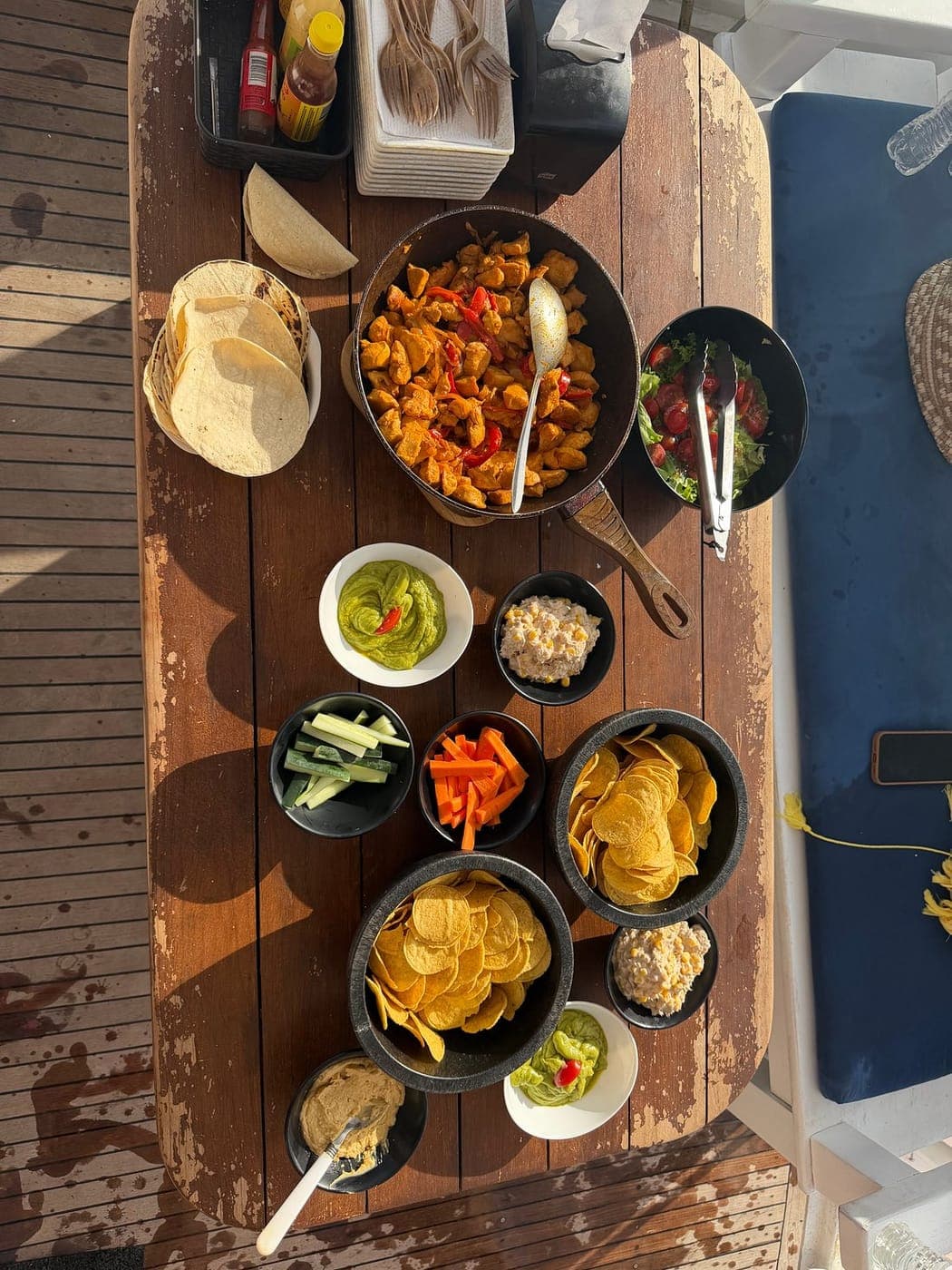 A spread of tortillas, guacamole, salsas and chips on a wooden table on deck, seen from above
