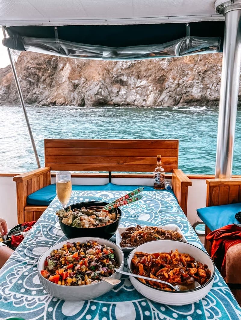 Bowls of food on a table under the deck awning, with a rocky headland behind