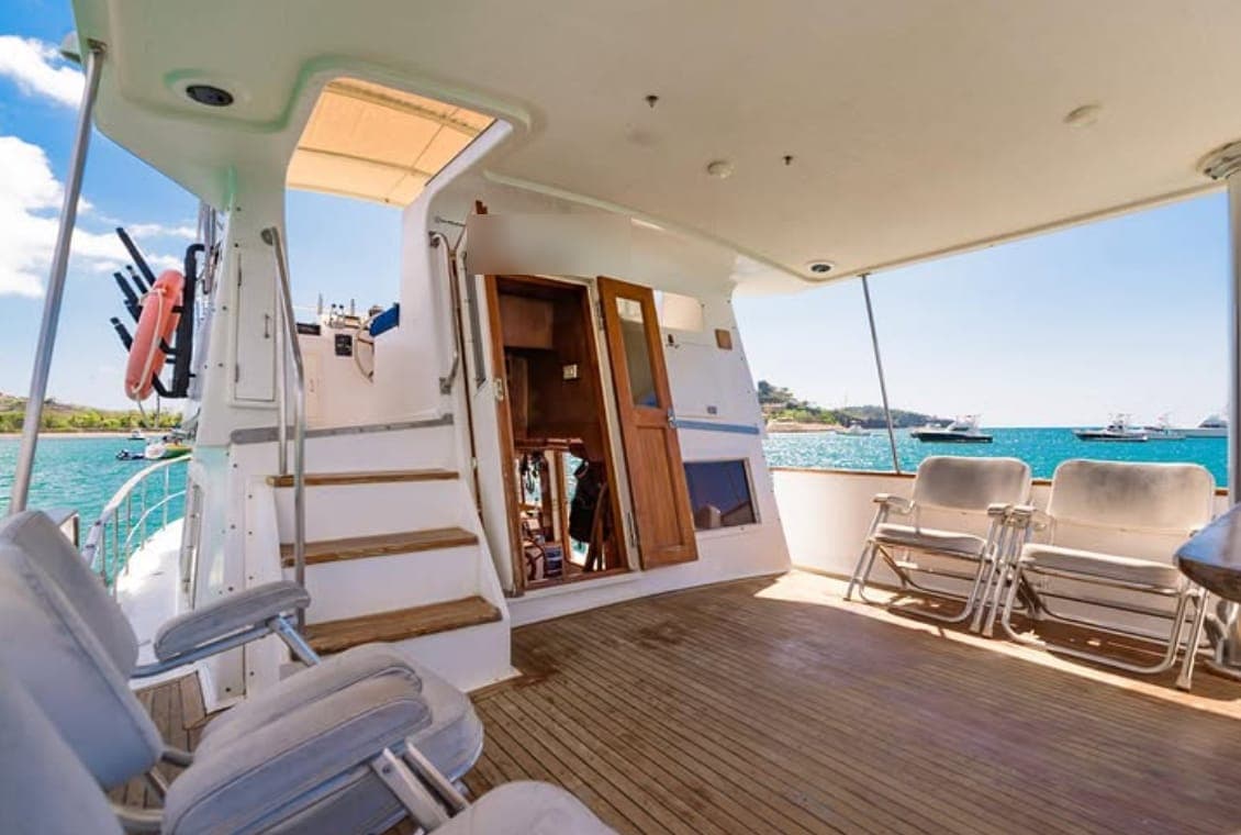 The shaded teak main deck with deck chairs, steps to the upper deck and the bay beyond
