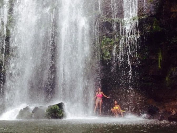Two people standing in the pool at the foot of a wide curtain waterfall
