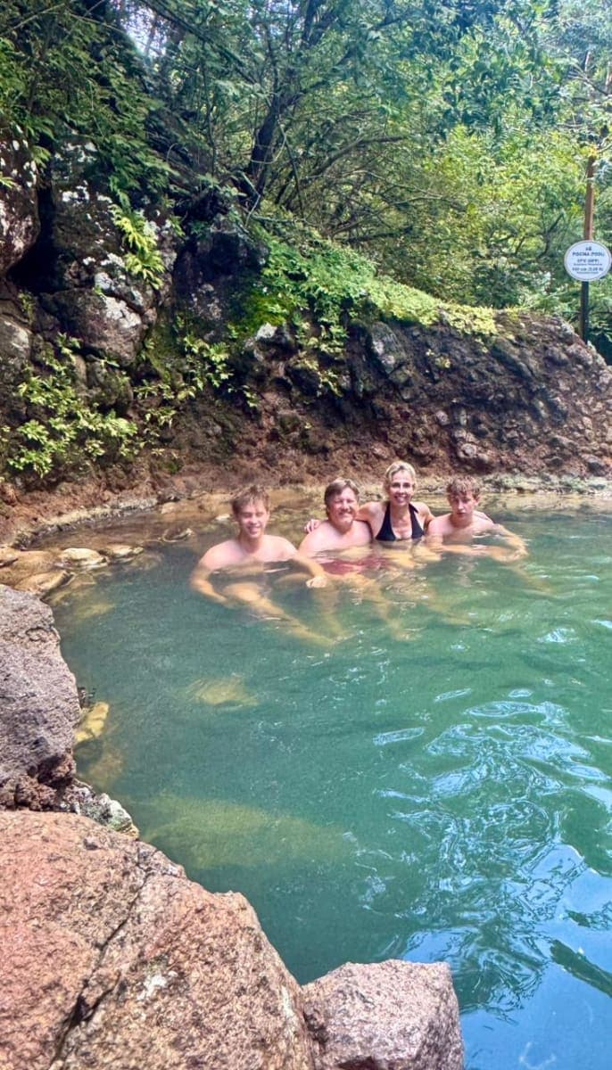 A group of guests relaxing together in a natural hot spring pool below a mossy rock wall