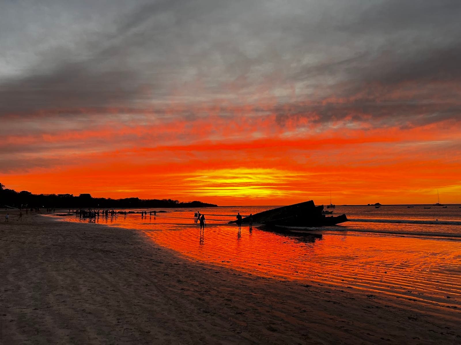 An orange sunset over a beach with the silhouettes of people on the sand